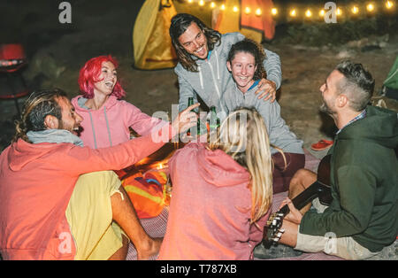 Gruppe von Freunden Spaß jubeln mit Bier am Strand mit Zelt in der Nacht - glückliche junge Leute Gitarre spielen und zusammen lachen Stockfoto