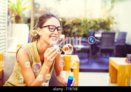 Glückliche junge Frau blasen Seifenblase in bar Restaurant - Schöne Mädchen Spaß im Freien - Glück, Freude und Jugend lifestyle Konzept Stockfoto