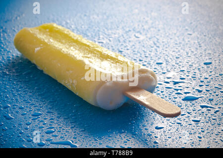 Gelbe Eis am Stiel oder Eis pop auf einem blauen Hintergrund mit Wassertropfen Stockfoto