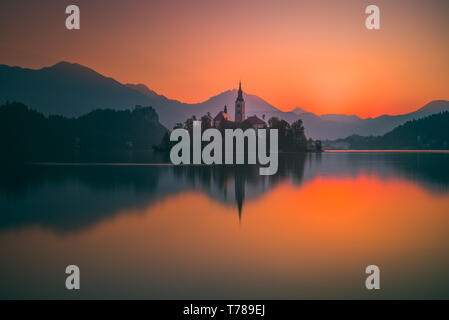 Kleine Insel mit ihn in Bled See, Slowenien bei Sonnenaufgang mit Schloss und die Berge im Hintergrund Stockfoto