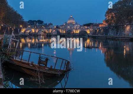 Tiber in Rom und der St. Peters Dom bei Nacht. Im Vordergrund ein versunkenen Schiff am Pier. Gebäude sind beleuchtet. Ufer mit Gebäuden und Stockfoto