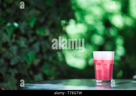 Trendy, hipster Kaffee. Ein Glas rosa Erdbeere Cappuccino auf die grünen Blätter Hintergrund. Frühling Stimmung. Stockfoto