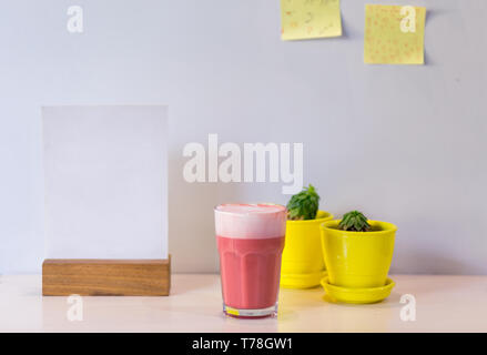 Trendgetränk, pink Kaffee Latte mit Schaum auf Tabelle mit gelben saftigen Töpfe in Cafe. Kopieren Sie Platz für Menü. Stockfoto