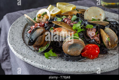 Meeresfrüchte schwarze Fettuccine fehttuchini. Schwarze Pasta mit Tintenfisch, Muscheln, Tintenfisch, Muscheln auf der Steinplatte. Gourmet Teller. Stockfoto