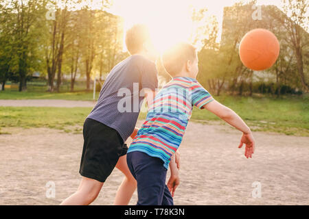 Zwei Jungen genießen Sie eine Partie Basketball herausfordernde einander für die Kugel von der hellen Hintergrundbeleuchtung flare von einem warmen Frühling Sonne hinter den Köpfen Stockfoto