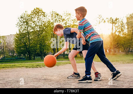 Zwei glückliche junge Boys Basketball spielen im Freien auf einem Sportplatz im Frühjahr mit Hintergrundbeleuchtung Stockfoto