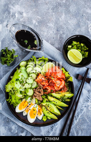 Lachs poke Schüssel mit Avocado, Eier, Gurken und Grünen serviert. Ansicht von oben mit der Kopie. Stockfoto