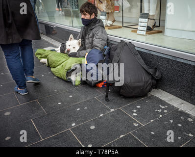 Obdachlosen Mann auf der Straße mit seinem Hund als Fußgänger vorbei. Stockfoto