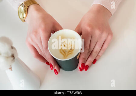 Auf der Cafe Tabelle weibliche Hände halten eine Tasse Kaffee mit einem Muster auf dem Schaumstoff Stockfoto