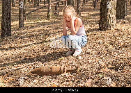 Kind mit Schrecken betrachtet einen rostigen nicht explodierte Bombe im Wald Stockfoto