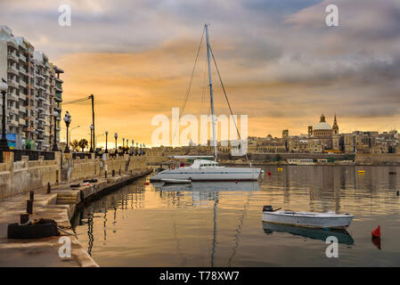 Klassische Postkarte Blick auf die Basilika Unserer Lieben Frau vom Berg Karmel und St Paul's Pro-Cathedral. Valletta, Malta. Himmel mit Wolken, Sonnenaufgang. Yacht- und Stockfoto