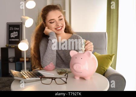 Junge Frau, Dollar, Banknote in Sparschwein im Innenbereich. Kosteneinsparungen Konzept Stockfoto