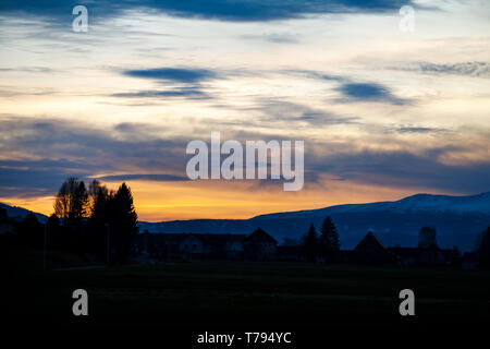 Sonnenuntergang mit verschiedenen Arten von Wolken und ein Berg und Tal Silhouette mit einem Gebäude in den österreichischen Alpen Stockfoto