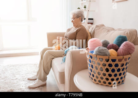 Ältere Frau sitzt auf dem Sofa, während Stricken Pullover zu Hause Stockfoto