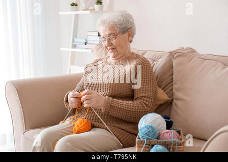 Ältere Frau sitzt auf dem Sofa, während Stricken Pullover zu Hause Stockfoto