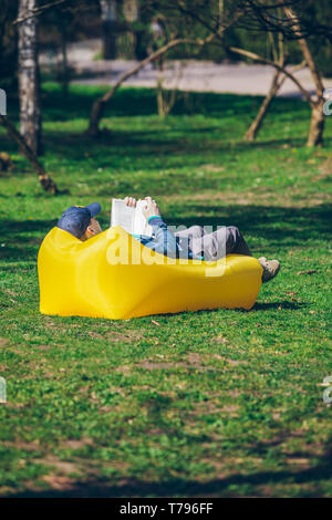 Buch Konzept. Mann im City Park auf aufblasbaren Matratze. Feder, sonnigen Tag Stockfoto