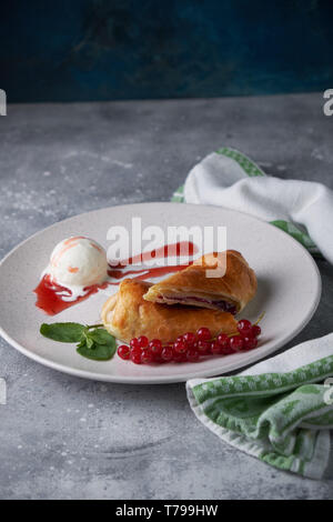 In Scheiben geschnittene Hausgemachte berry Strudel mit frischen rote Johannisbeere Beeren und Puderzucker auf einem alten Hintergrund auf einer Platte mit Eis pic serviert. Stockfoto