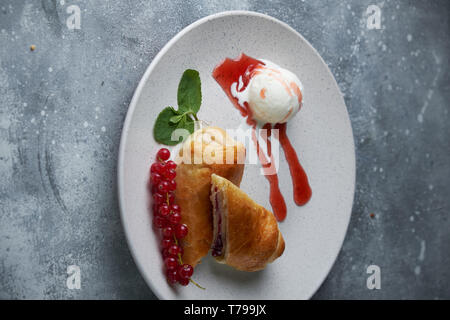 In Scheiben geschnittene Hausgemachte berry Strudel mit frischen rote Johannisbeere Beeren und Puderzucker auf einem alten Hintergrund auf einer Platte mit Eis pic serviert. Stockfoto