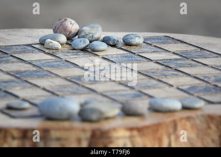 Ein Schachbrett geschnitzt in einem Baumstumpf, durch natürliche, glatten Stein Spielsteine akzentuiert. Stockfoto