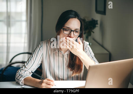 Ein Mädchen arbeitet an einem Computer in einem Home Office oder ein Student zu Hause Lektionen unterrichtet. Müde ist, gähnt und will schlafen, oder ist langweilig. Stockfoto