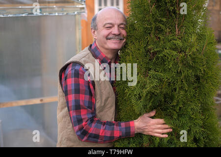 Reifer Mann ist stolz auf seinen Garten und umarmte seinen lieblingsbaum Stockfoto