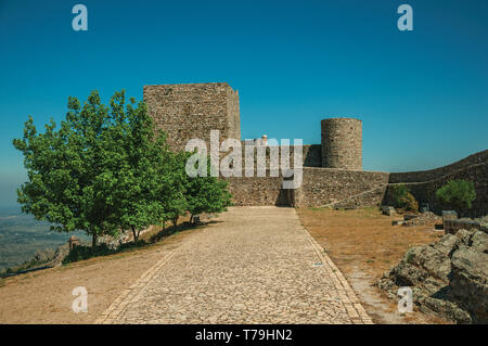 Weg mit Bäumen zu dicke Steinmauern und quadratischen Turm an der Marvao Castle. Eine mittelalterliche Weiler thront auf einem Felsen in Portugal. Stockfoto