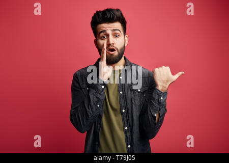 Super Kerl mit einem Palm auf seinem Mund, Klatschen, Flüstern etwas an der Kamera an. Schließen Sie herauf Foto. Kerl erzählt ein Geheimnis. chatterbox Stockfoto
