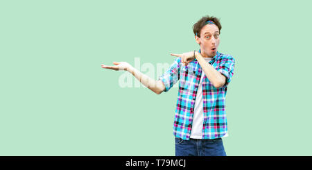 Portrait von überrascht junger Mann in casual blau kariertem Hemd und Stirnband mit Kamera mit entsetzten Gesicht und etwas an der Wand. Stockfoto