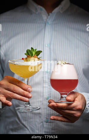 Barkeeper enthält zwei verschiedene Sommer Cocktails in Händen. Rote und gelbe Getränke in barman Hände. Vertikale. Kopieren Sie Platz Stockfoto