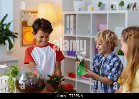 Junge Beregnungswasser. Blond lustig junge beregnungswasser auf seine Mitschüler nach der Bewässerung pflanzen Ökologie Klasse Stockfoto