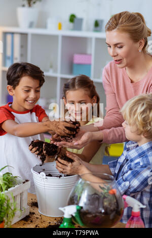 Schön Botanik Lektion. Jungen und Mädchen, die an Botanik Lektion Gefühl fröhlich mit Lehrer während Blumenerde Pflanzen Stockfoto