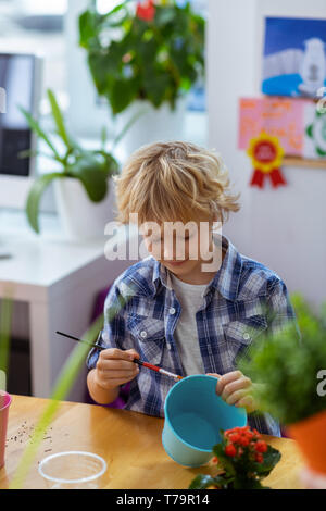 Färbung Blumentopf. Blonde Schüler tragen Squared shirt Färbung Blumentopf für seine Home Anlage Stockfoto