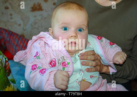 Porträt einer überrascht vier Monate altes Baby Mädchen mit blauen Augen in die Arme ihrer Mutter sitzen Stockfoto