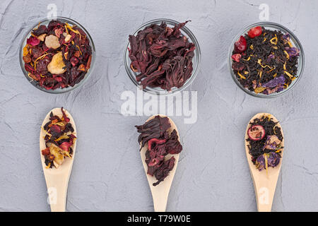 Schüsseln und Löffel mit getrockneten Teeblätter. Verschiedene Arten von trockenen Kaffee auf grauem Hintergrund. Aromatische Zutaten für gesundes Getränk. Stockfoto
