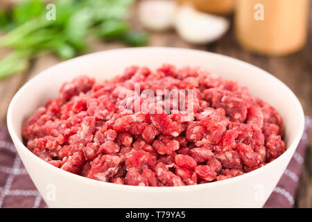 Frische rohe Masse oder Hackfleisch, Fleisch in der Schüssel, Gewürze (Salz, Pfeffer), Knoblauch und Petersilie auf der Rückseite (selektive Fokus) Stockfoto