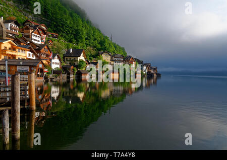 Am frühen Morgen geschossen von Hallstatt Häuser und Reflexionen im Wasser der Hallstätter See (Hallstätter See) mit niedrigen Wolken im Hintergrund Stockfoto