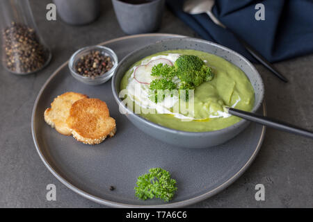 Seitenansicht Diät Cremesuppe mit Brokkoli und Sauerrahm mit Radieschen, Löffel, Pfeffer und Serviette in der Nähe von auf Beton grau hinterlegt. Konzept der Diät Sommer Stockfoto