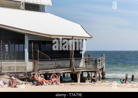 Melbourne, Victoria/Australien - 06 Februar 2019: Jung und Alt genießen Sie einen warmen Sommertag durch das Sitzen auf St. Kilda Beach Front, während die Wellen sanft am Strand schoß. Stockfoto