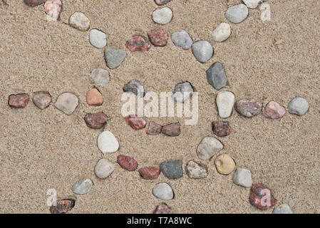 Sun Form aus Kieselsteinen auf Sand Hintergrund Textur Stockfoto