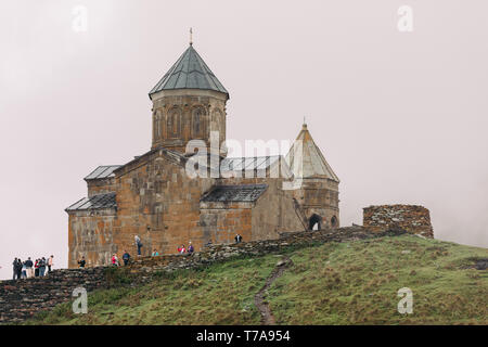 Trinity Kirche von Gergety, Georgien - 17. September 2018: Touristen in der Nähe der Trinity Church von Gerget an einem regnerischen Herbsttag, Georgien Stockfoto