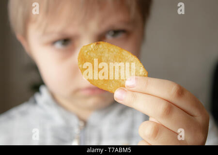 Das Kind ist mit Chips. Close-up. Der Junge schaut auf die Chips. Junk Food. Stockfoto