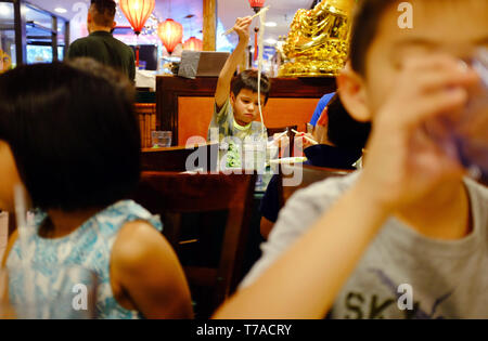 Ein Junge mit Stäbchen herauf Nudeln aus seine Schale in einem Chinesischen Restaurant in Chinatown. Manhattan, New York City.NY USA Stockfoto