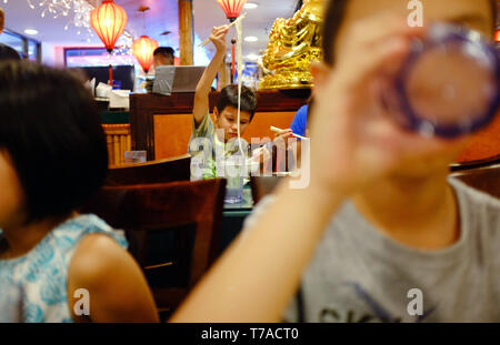 Ein Junge mit Stäbchen herauf Nudeln aus seine Schale in einem Chinesischen Restaurant in Chinatown. Manhattan, New York City.NY USA Stockfoto