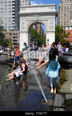 Menschen Abkühlung im und durch den Brunnen des Washington Square Park mit Washington Square Arch im Hintergrund. New York City, USA. Stockfoto