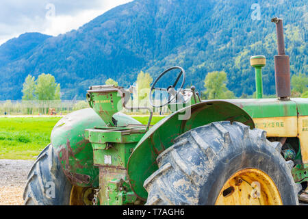 Alte John Deere Traktor mit rostigen, verschmutzte Teile der Maschine. Das Sitzen auf einem Bauernhof. Große Räder des Schleppers angezeigt. Abgenutzte Logo auf der Farm Equipment. Stockfoto