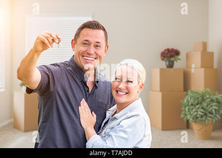 Glückliches Paar mit neuen Hausschlüssel im leeren Raum mit Boxen. Stockfoto