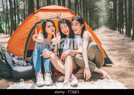 Gruppe der glücklichen asiatischen Mädchen im Teenageralter dabei Sieg zusammen stellen, Camping, das sich vom Zelt. Aktivität im Freien, Abenteuer Reisen oder Urlaub Konzept Stockfoto