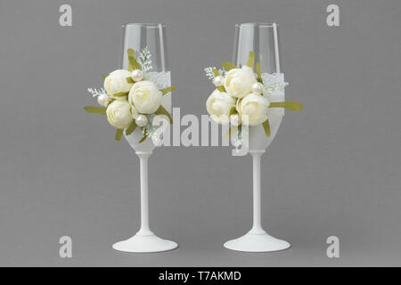 Zwei Hochzeit Weingläser mit Spitze und weißen Rosen auf grauem Hintergrund eingerichtet. Stockfoto
