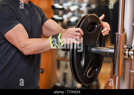 Closeup Schuß von nicht identifizierbaren muskulösen Mann herauf schwere Hantel Gewichte von Rack im modernen Fitnessraum. Stockfoto