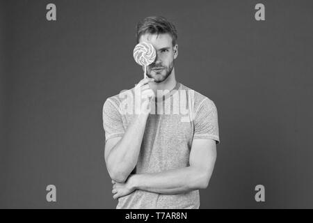 Mann mit Borsten mag Lollipop. Cheat meal Konzept. Zucker schädlich für die Gesundheit. Kerl halten Lollipop candy violett unterlegt. Geschmack der Kindheit. Lollipop Spaß. Mann essen großen bunten süßen Lutscher. Stockfoto